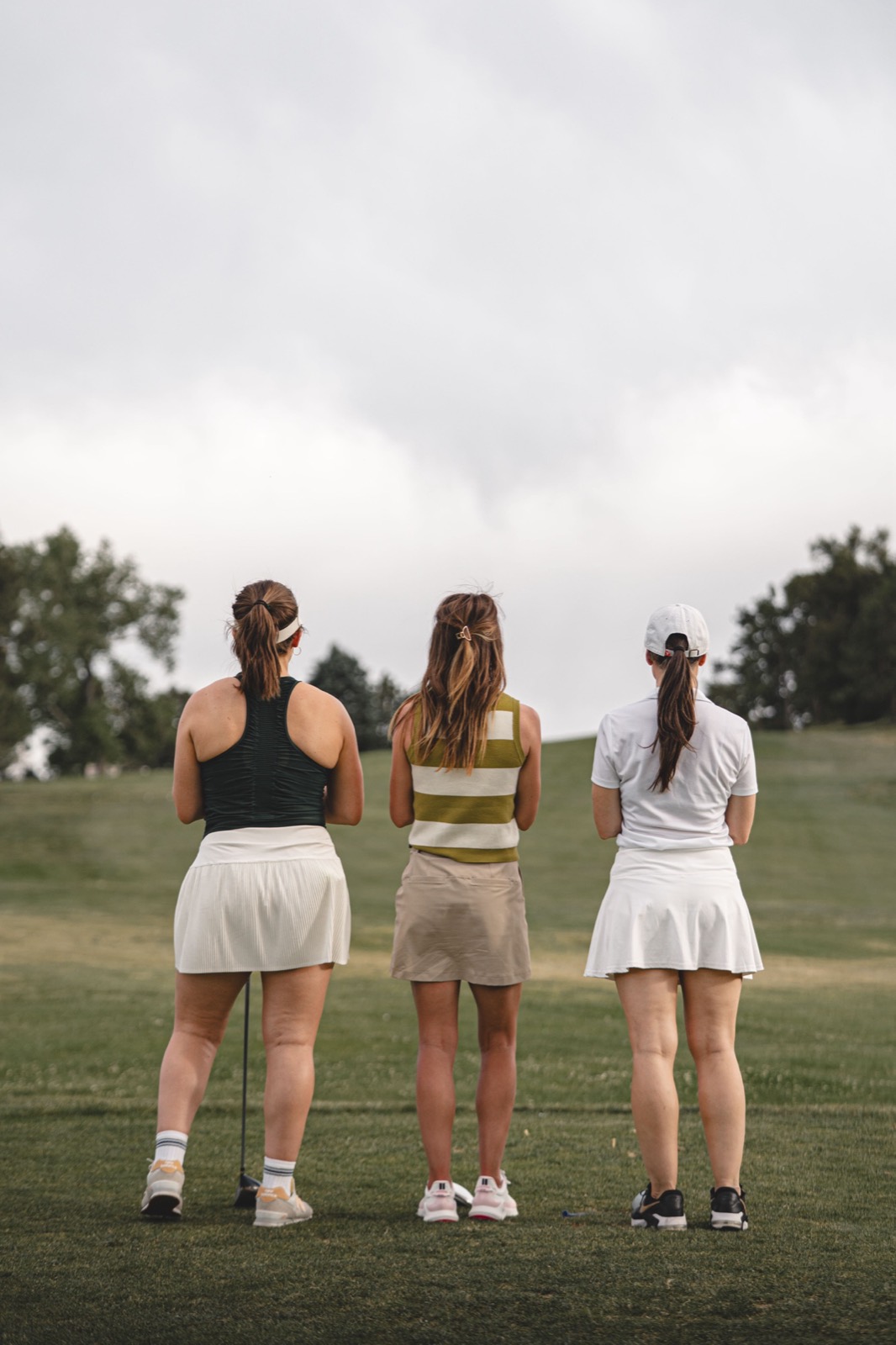 Three women standing side by side on the course, watching the fairway ahead