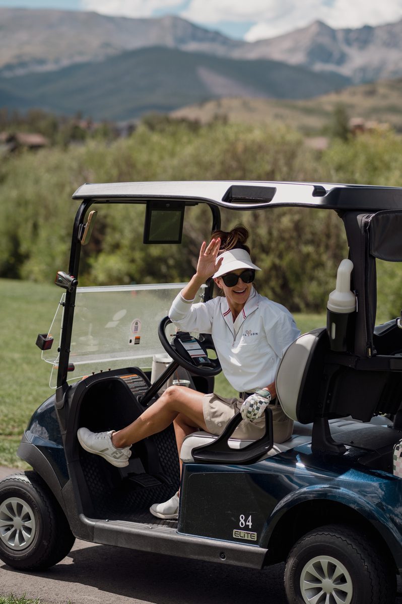 A player waving from her golf cart with the mountains behind her