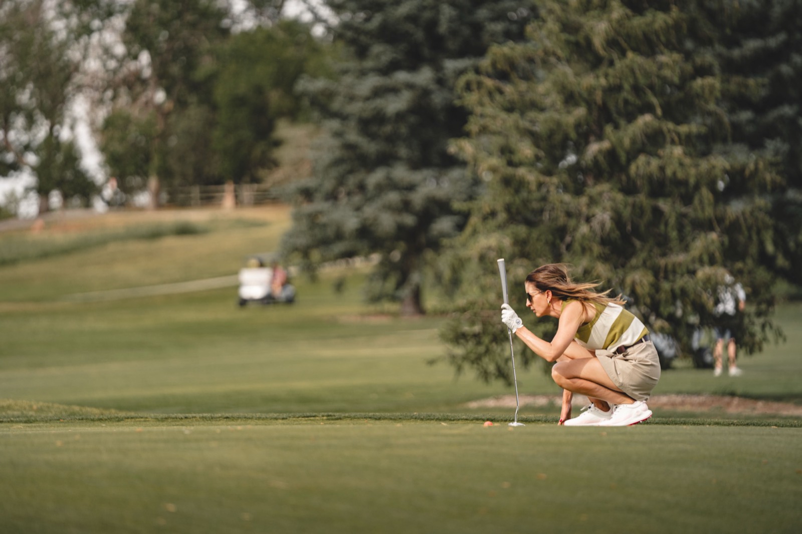 A woman crouched on the fairway reading her next shot in warm evening light