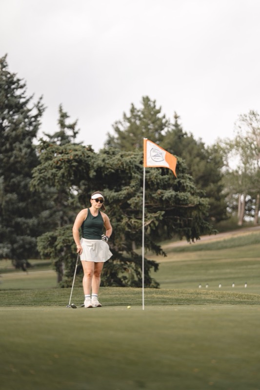 A woman lining up a putt beside the flag