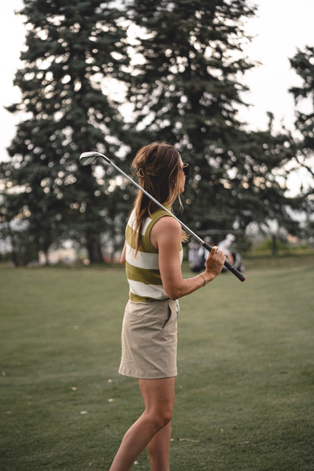 A woman resting a club across her shoulders between shots on the course