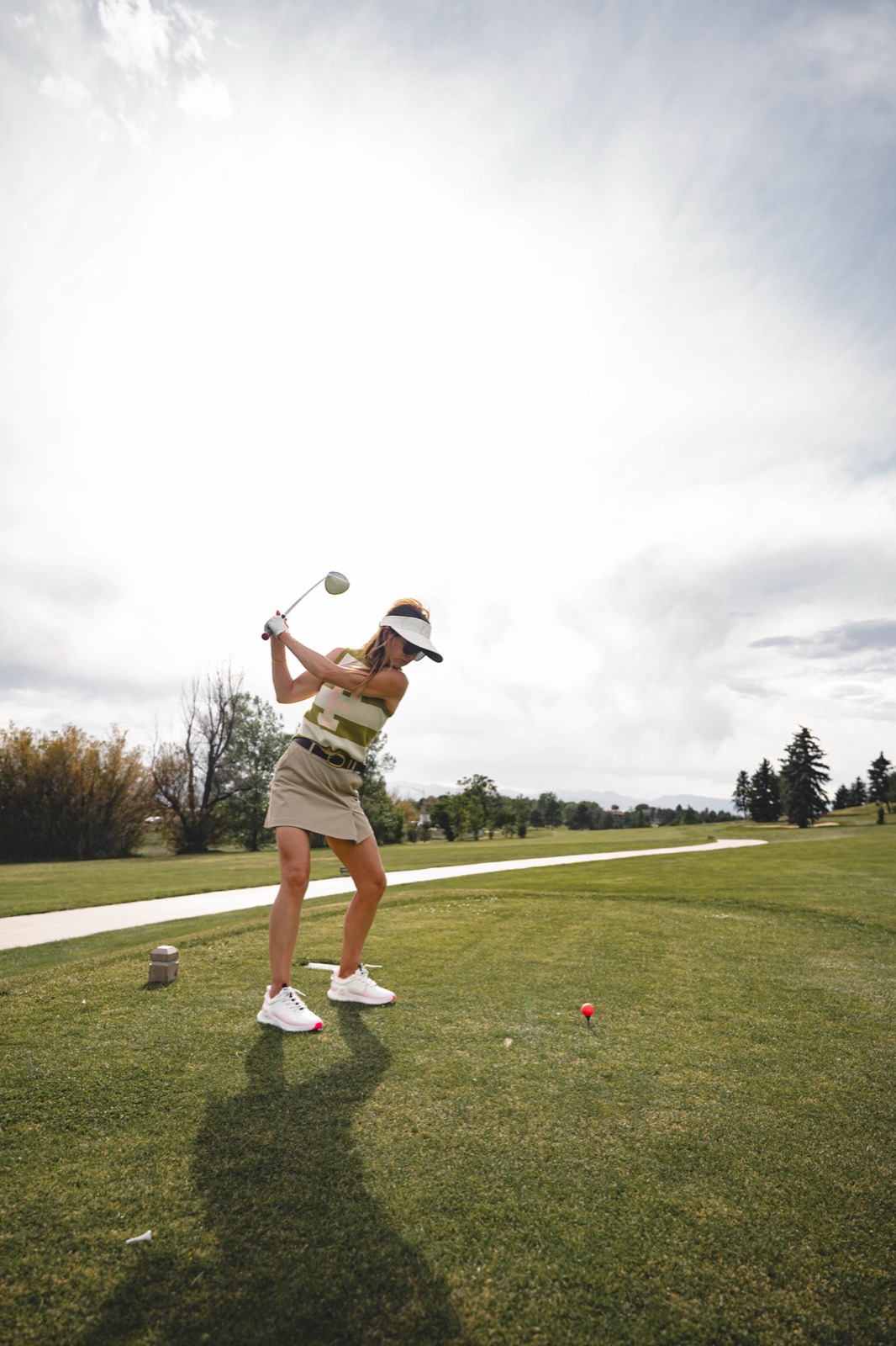 A woman mid-swing on the tee, framed against a bright open sky